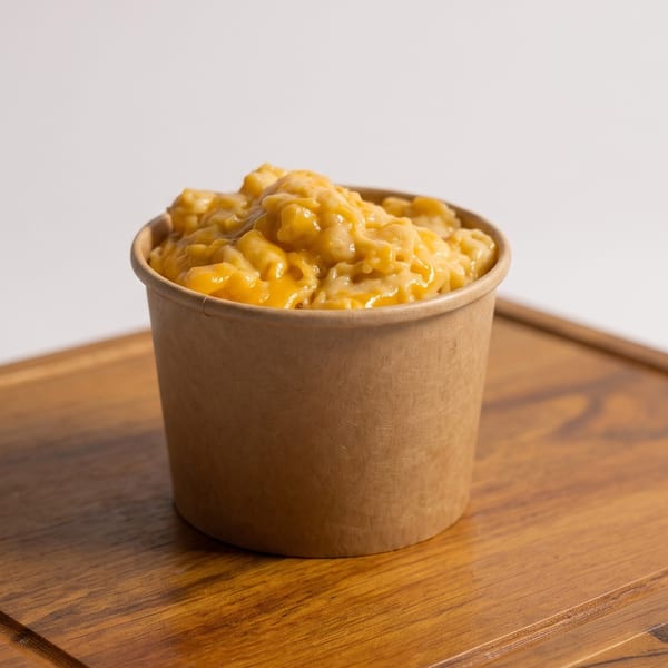 Creamy mac and cheese in a disposable brown cup on a wooden board.