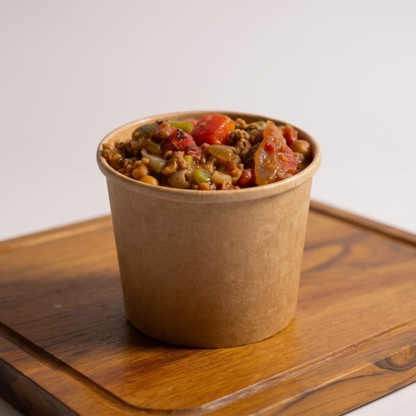 Lentil and vegetable stew in a brown paper cup on a wooden board.